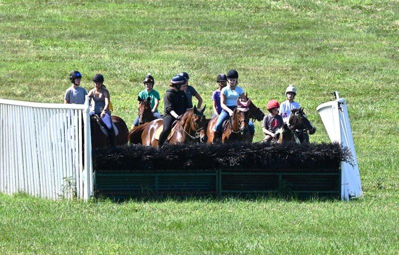 group of young riders on horses standing at a steeplechase fence